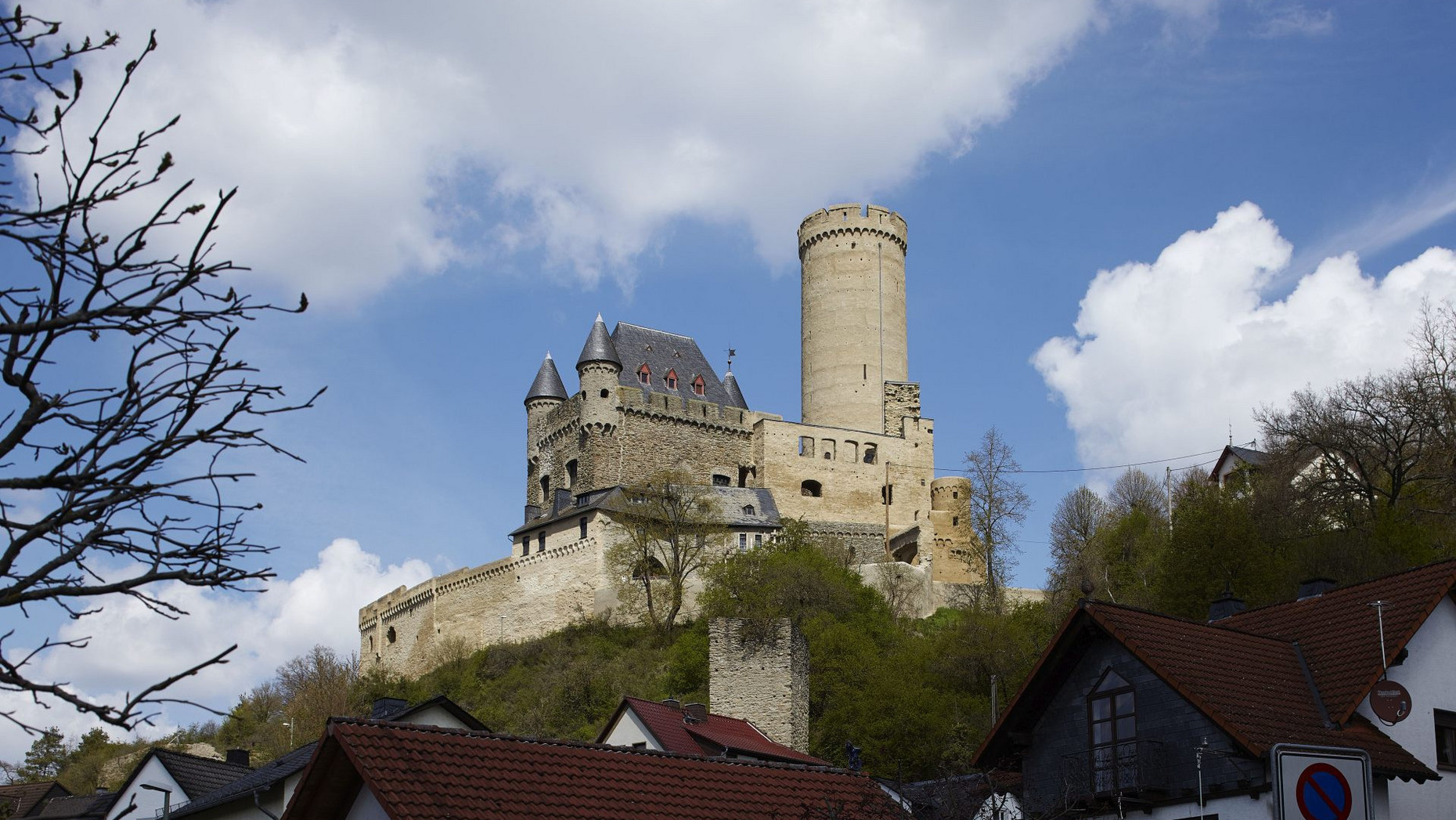 Burg Schwalbach Ansicht der Burg Schwalbach, Bergfried rechts vor blauem Himmel mit Wolken, links im Vordergrund und rechts Bäume, ein Wohnhaus.