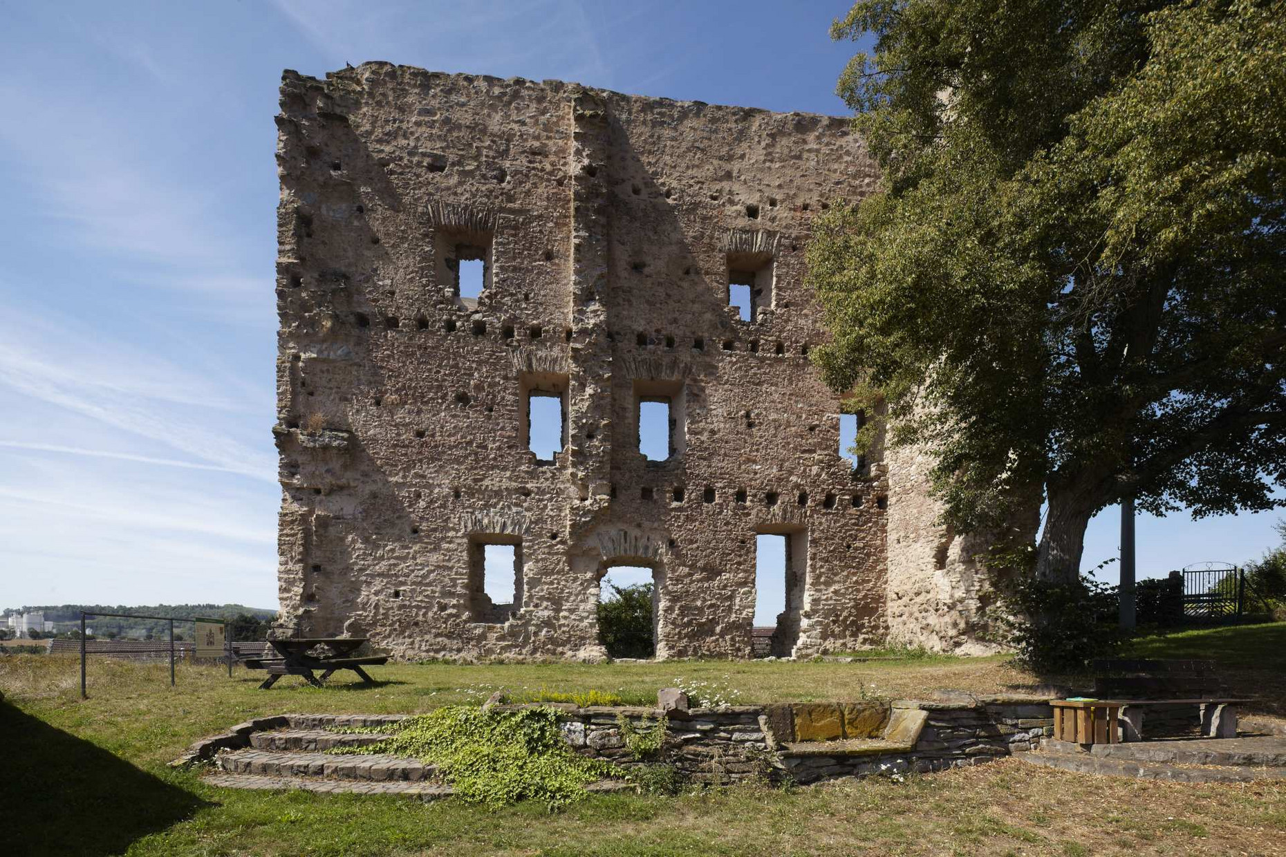 Oberneisen Mauerwand, Tisch mit Bank und Stufen im Vordergrund, rechts ein Baum und ein Tor